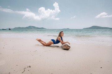 Fototapeta na wymiar Young attractive blonde woman in a blue swimming suit lying on a sandy beach against the sea background. Summer vacation concept