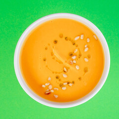 Pumpkin soup in white plate on green background. Close-up. Top view. Space for text. Photo for cutting, for menu