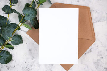 Blank white card, envelope and eucalyptus branch on white marble background. Blank invitation. Flat...