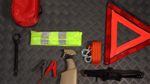 Closeup top view 4k stock video footage of many tools and equipment need for safe driving by car. Different objects laying on black rubber protective rug inside of boot of automobile. Emergency kit