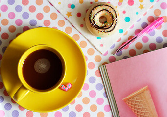 yellow cup with coffee, donut and notebook with a pen lie on a colorful background