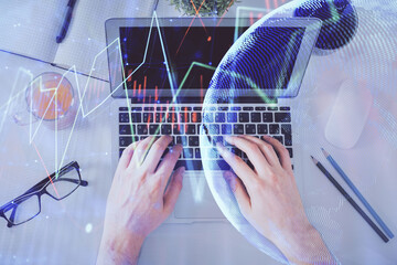 Double exposure of man's hands typing over laptop keyboard and forex chart hologram drawing. Top view. Financial markets concept.