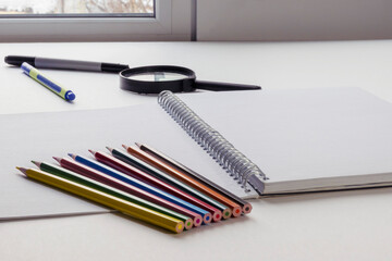 Pencils of different colors lie on an open drawing notebook. Copy space.