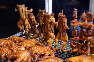 Whole frog on grill, night street food closeup. Exotic meat grill. Frog kebab on stick closeup. Octopus and frog meat roasted