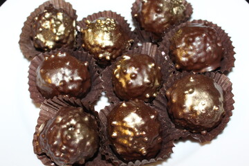 Chocolate nut cakes are on a white plate. They are decorated with gold dust and wrapped in paper wrappers.