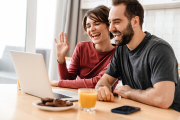 Happy young couple smiling and using laptop while sitting at home