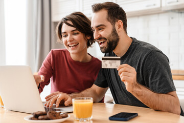Happy young couple using laptop and credit card while sitting at home