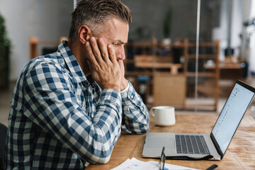 Tired grey man working with laptop while sitting in office