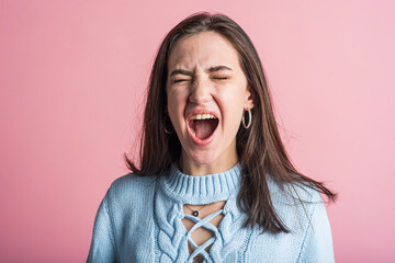 Portrait of a brunette girl who screams after a quarrel in the studio on a pink background