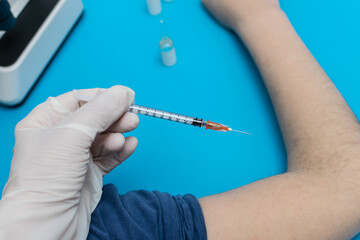 
Nurse or male nurse hand holding vaccine syringe for injecting into Caucasian child arm on laboratory table next to vials and microscope on blue background.