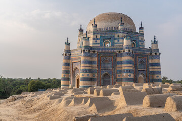 Landscape sunset view of beautiful ancient medieval blue tomb of Bibi Jawindi with traditional graveyard in foreground in Uch Sharif, Bahawalpur, Punjab, Pakistan