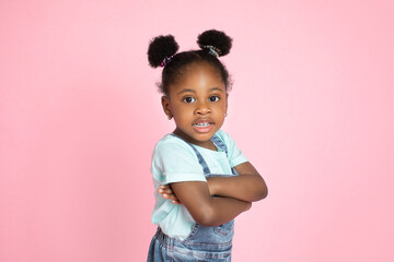Little african-american girl's portrait on pink studio background. Happy cute girl, standing with...