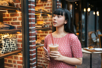 Asian thai long dark hair woman with ice coffee and smartphone in Bangkok street.