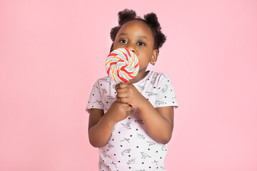 Close up of cute happy little African girl with lollipop candy in front of colorful pink background with copyspace