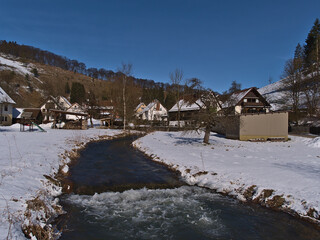 Idyllic winter landscape of small rural village Gundelfingen, part of Münsingen, Germany in Swabian Alb with Große Lauter river, snow-covered meadow and residential houses on sunny day with blue sky.