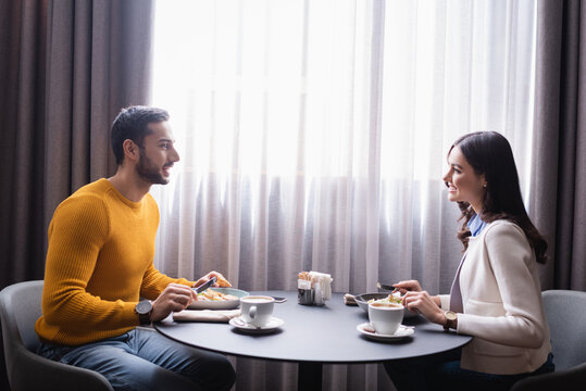 Cheerful interracial couple looking at each other while dinning in restaurant