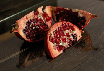 Three slices of the cut pomegranate lie on a wooden board. Dark background.
