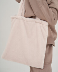 Grey textile bag hanging at female shoulder. Woman in beige hoodie
