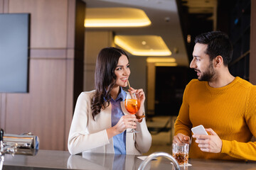 Cheerful multicultural friends with drinks and smartphone spending time in restaurant