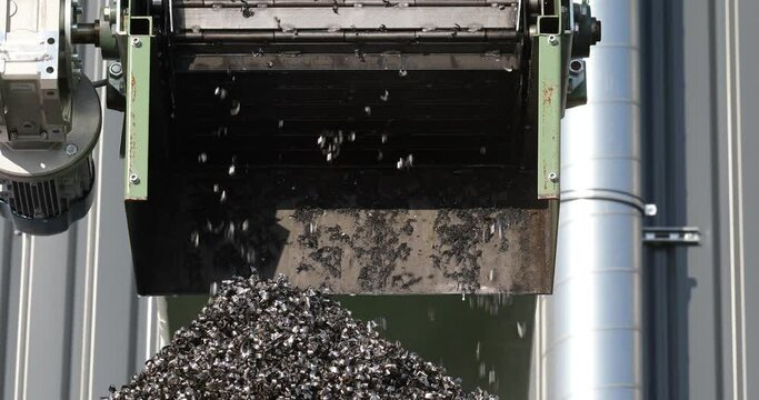 Metal pieces falling into a box from recycling processing machine. Recycled scrap metal in stock. Metal shavings production waste