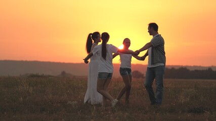 Fototapeta na wymiar A happy family, a young mother, dad and daughters play and dance together in the sun, have fun in field. Children with parents play in park on grass at sunset. Happy family childhood and health