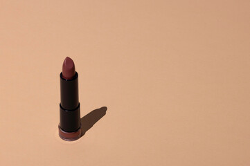 Lipstick on a beige background with hard shadow. Female cosmetic product for makeup. Copy space.