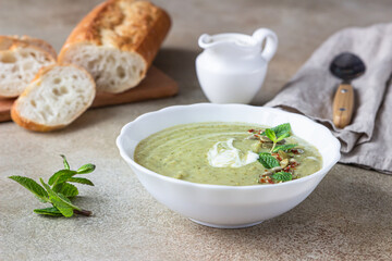 Broccoli cream soup served with mint, cream, seeds and fresh bread on concrete background. Healthy vegetarian food concept.