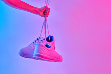 Hand hold white sneakers in neon light. Sport shoes for training in the gym. Creative minimalism....