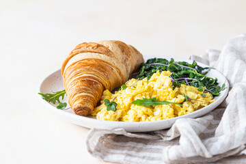 Croissant served with scrambled eggs and spinach on plate, light concrete background. Breakfast.