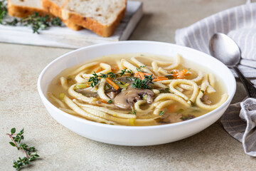 Vegan noodles soup with mushrooms and vegetables served with thyme, light concrete background.