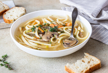 Vegan noodles soup with mushrooms and vegetables served with thyme, light concrete background.