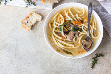 Vegan noodles soup with mushrooms and vegetables served with thyme, light concrete background. Top view.