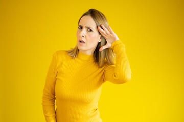 Young woman over isolated yellow background listening to something by putting hand on the ear