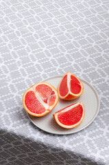 Vertical image.Pieces of grapefruit on the grey plate and tablecloth on the kitchen table.Empty space