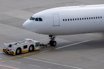 The apron transporter tows a modern narrow-body white passenger aircraft across the airfield of an international airport.