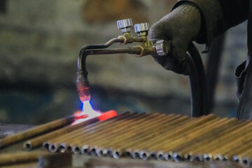 A man's hand holds a metal cutting torch and warms pipes with it