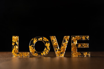Acrylic letters with gold leaves forming the word love on wooden surface, black background,...