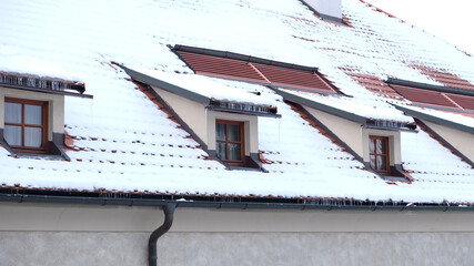 Exterior of apartments with gable roofs and dormers covered with snow in winter. City building view...