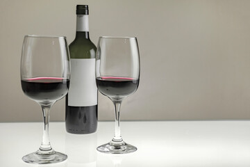 Two large glasses with red wine and a bottle on a blurred background, close-up. Horizontal photo