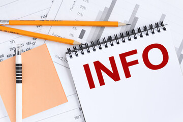 Info. text on a white notepad on a light background next to financial charts and a sticker.