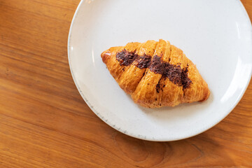 French chocolate croissant on plate on wooden table and nature sunlight with shadow through from window