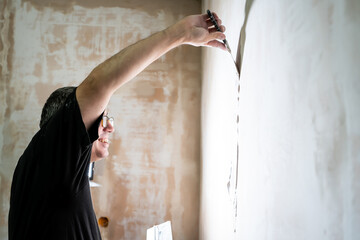 Manual worker with wall plastering tools renovating house. Plasterer renovating indoor walls and...