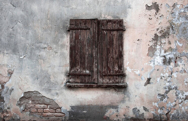 Fototapeta na wymiar Window closed with old wooden shutters on the background of peeling wall