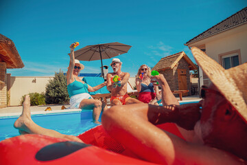 Obraz na płótnie Canvas Senior friends having fun playing with water guns at the swimming pool