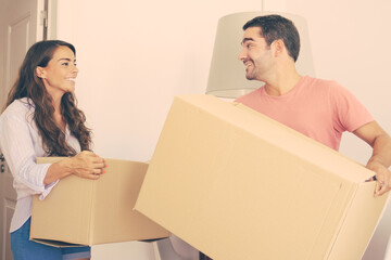 Happy young couple moving into new apartment, carrying carton boxes, looking around and smiling....