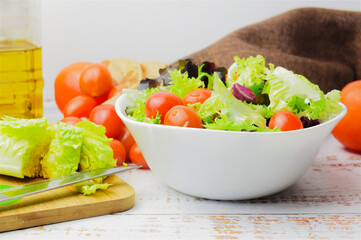 In white bowl, mixed salad, accompanied by small tomatoes.