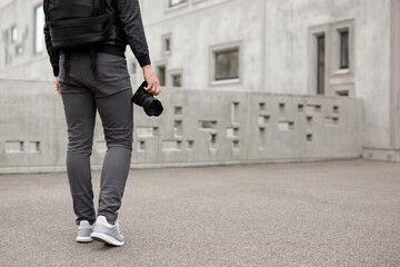 back view of male photographer walking with modern dslr camera over concrete building background