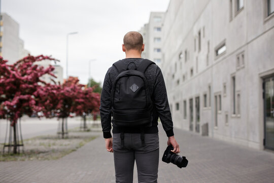 back view of male photographer with modern dslr camera walking at the street