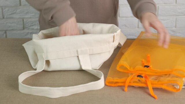 Woman with cloth bags in the kitchen. The female folds her eco-friendly reusable bags into a cotton shopping bag.