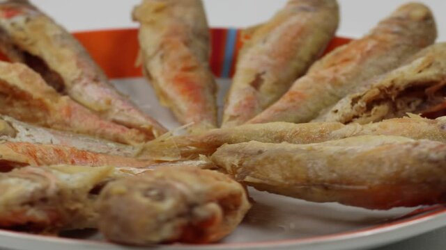 A closeup of cleaned and fried fresh small mullets on a plate in 4K